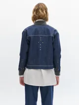 Campera de denim azul oscuro con cuello redondo, cierre frontal con botones metálicos y tachas plateadas en el frente y la espalda.