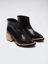 Botineta de cuero color suela, con diseño de punta fina y puntera texturizada con efecto reptil. Presenta una suela de madera clara con borde negro y cierre lateral interno.