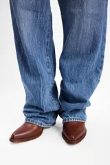 Bota estilo western de caña media, confeccionada en gamuza color marrón con bordados decorativos en hilo claro. Cuenta con taco cuadrado de madera y tiradores laterales.