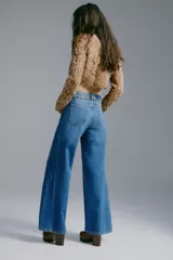 Jean de tiro alto y corte acampanado, confeccionado en denim de algodón. Presenta diseño de cinco bolsillos, cierre frontal con botón y costuras decorativas laterales.