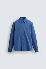 Camisa de corte regular fit confeccionada en tejido de algodón con textura. Presenta cuello solapa, cierre frontal de botones, manga larga con puños abotonados y un bolsillo plastrón en el pecho.