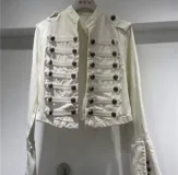 Chaqueta de denim estilo militar con cuello mao, cierre frontal con botones metálicos y detalles de trabillas horizontales. Presenta hombreras decorativas y diseño estructurado.