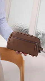 Neceser de símil cuero color marrón con doble compartimento superior y bolsillo frontal con cierre. Cuenta con un asa lateral para transporte y el logo de la marca Lincoln's grabado en el frente.