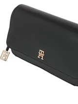 Cartera cruzada negra de poliuretano con diseño estructurado y solapa frontal con cierre magnético. Posee correa larga ajustable, bolsillo interior y herrajes metálicos dorados, incluyendo un monograma TH en la solapa y un charm colgante con el logo.