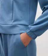 Campera deportiva de modal negro con capucha, cierre frontal por cremallera, cordones ajustables, bolsillos y mangas largas con puños elásticos.