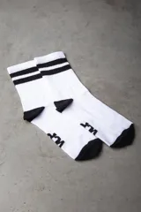Medias deportivas blancas con dos rayas negras en la parte superior, talón y puntera negros, y detalle de letras estampadas en la planta.