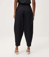 Pantalón de sarga de corte barrel, color negro, con pliegues en la cintura, piernas amplias y botamangas afinadas.
