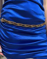 Cinturón tipo caderín de diseño trenzado, elaborado en metal con acabado brillante dorado y textura escarchada. Cuenta con un cierre de hebilla metálica rectangular.