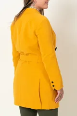 Chaqueta cruzada color mostaza con lazo y botones negros. Tiene bolsillos con tapa y detalle de cuatro botones en las mangas.