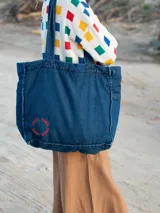 Bolso tote de denim azul oscuro con bordado circular rojo.