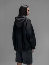 Hoodie oversize color negro, confeccionado en frisa gamuzada de algodón con recortes en hombros y bolsillo frontal tipo cargo con solapa en material técnico. Presenta capucha forrada y puños y ruedo acanalados.