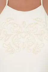 Malla enteriza color beige con cuello halter alto, tirantes para anudar al cuello, detalle de bordado con cuentas en el pecho y fruncidos en los laterales.