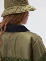 Campera tejido grueso y abrigado color verde militar, con forro de nylon interno, cuello estilo camisa en color negro y cierre frontal con botones. Cuenta con cuatro bolsillos delanteros con apliques en distintos tonos y texturas, y un parche bordado circular en el bolsillo superior izquierdo.