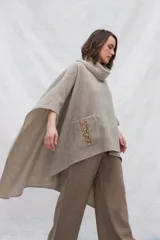Poncho de lana color beige con cuello alto, bolsillos frontales y detalle de cordones de cuero en los bordes de los bolsillos.