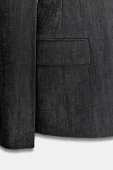 Blazer de mujer color gris oscuro, con efecto denim o tejido texturizado. Presenta cuello solapa de muescas, hombreras, bolsillos con solapa en el delantero y cierre frontal de dos botones oscuros.