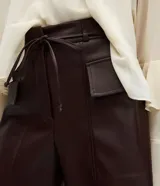 Short de poliuretano color marrón oscuro, con cintura fruncida en la parte trasera, bolsillos delanteros amplios con solapas estructuradas y acabado brillante.