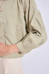 Cazadora azul de manga larga con puños elásticos, cuello redondo sin solapas y cierre frontal con botones grandes de color claro.