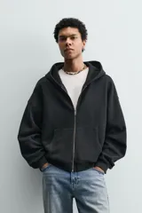 Sudadera tipo hoodie de corte relajado, confeccionada en tejido de algodón con textura estructurada y efecto lavado. Presenta cierre frontal con cremallera, cuello con capucha, manga larga, bolsillos tipo canguro y acabados en rib.