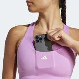 Top deportivo Adidas de soporte medio, color lila, con cuello redondo, espalda cruzada y múltiples bolsillos ocultos. Presenta el logo de Adidas en blanco en el pecho.