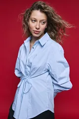 Camisa blanca de manga larga con volumen y estructura, cierre frontal con botones y lazo ajustable en la cintura que realza la silueta.