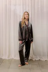 Pijama de tela velvet color gris oscuro, compuesto por una camisa de manga larga con botones y vivo en contraste rojo, y un pantalón recto con elástico en la cintura.