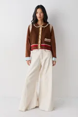 Chaleco de lana color marrón con cuello estilo bebé, cierre frontal con botones grandes y detalle de puntilla en cuello, sisas y bolsillo frontal. Presenta una franja decorativa en color rojo en el ruedo.