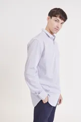 Camisa de manga larga, color rosa claro con finas rayas verticales blancas, cuello camisero y un bolsillo en el pecho.