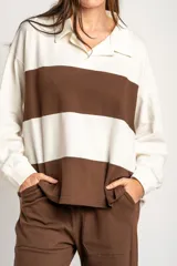 Sweater de tejido de punto con diseño a rayas horizontales en color crema y marrón. Presenta cuello tipo polo con cierre frontal de botones ocultos, mangas largas y un corte oversize.