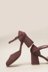 Zapato de tacón color bordó, confeccionado en terciopelo suave, con diseño de pulsera en el tobillo y cierre de hebilla. La punta es cerrada y presenta detalles de líneas cosidas. El tacón es ancho y forrado, con una altura de 7 cm.