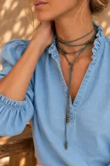 Gargantilla y collar corbatín de tiento de cuero color gris, con cuentas metálicas doradas distribuidas a lo largo del diseño.