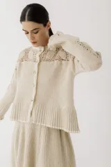 Saco de punto color beige, con diseño de calados en la parte superior y mangas, cierre frontal con botones y cuello redondo.