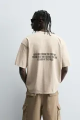 Camiseta de corte relaxed fit, color beige claro con efecto lavado, cuello redondo y manga corta. Estampado frontal en negro con texto "SUNSET ERA" y un caballo galopando.