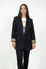 Blazer negro de corte clásico con solapas redondeadas y bolsillos con solapa. Presenta un detalle distintivo de estampado animal print en el interior de los puños, visible al doblar las mangas.