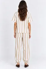 Blusa de manga corta a rayas beige y blancas, con cuello mao y cierre frontal de botones con trabillas (alamares). Cuenta con tajos laterales.