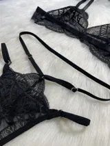 Conjunto de lencería de cuatro piezas en encaje negro, compuesto por bralette, tanga con tiras regulables, portaligas y ligas para piernas.