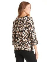 Blusa de algodón con estampado ikat en tonos blanco, negro y marrón. Presenta cuello a la base con escote en V y un patrón geométrico bordado. El estampado se realza con sutiles tachas doradas. Mangas tres cuartos con puño ancho y pequeña abertura lateral. Ruedo con tajos en los costados.