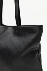 Cartera tote negra de símil cuero con diseño texturizado de parches y asas largas.
