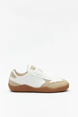 Zapatilla urbana de mujer, estilo minimalista y barefoot, en color blanco y beige con suela de goma marrón. Presenta paneles superpuestos en cuero liso y gamuza.