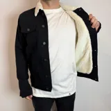 Chaqueta de jean negra con cuello de corderito blanco, cierre frontal con botones metálicos y bolsillos frontales con solapa.