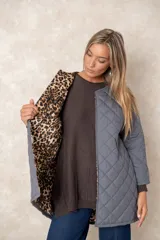 Campera acolchada de corte amplio y largo midi, color beige con diseño capitoneado. Presenta mangas tres cuartos con puños vueltos que revelan un interior estampado con motivo animal print. Diseño sin cuello y cierre frontal oculto.