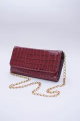 Cartera tipo sobre con textura de cocodrilo en color bordó, confeccionada en cuero. Cuenta con una cadena metálica dorada extraíble y múltiples compartimentos interiores, incluyendo un bolsillo con cierre para monedas.