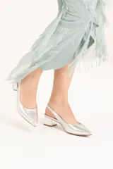 Zapato plateado de cuero sintético con punta fina, talón descubierto y taco cuadrado bajo.