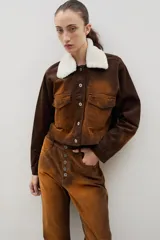 Chaqueta corta de pana con efecto gastado, cuello de corderito blanco desmontable, cierre frontal con botones metálicos y dos bolsillos frontales con solapa.