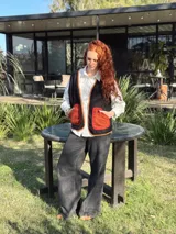 Chaleco negro con interior de corderito, con detalles en color naranja y ribeteado en marrón.