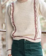 Sweater artesanal tejido a mano en lana merino, de color marfil con detalles en bordó. Presenta cuerpo delantero en crochet con guardas laterales decorativas y espalda en punto jersey, con cuello redondo y puños acanalados en contraste de color.