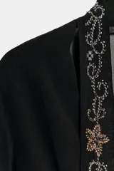 Camisa semitransparente negra de viscosa, con escote en pico pronunciado y manga larga con volantes. Incluye un foulard del mismo tejido con bordados florales y abalorios a contraste en tonos dorados y plateados.