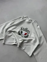 Buzo de corte boxy color crudo, con cuello redondo y mangas largas de hombros caídos. Presenta un estampado frontal con el logo de la marca, un escudo con los colores de la bandera italiana y detalles de laureles.