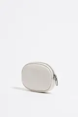 Monedero ovalado color blanco de la marca Bimba y Lola, confeccionado en piel. Cuenta con cierre de cremallera, tirador metálico, logo estampado y ribetes metálicos.