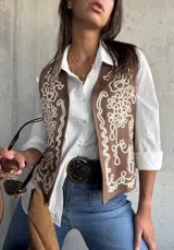 Chaleco de color beige con bordados decorativos en color crema en los paneles frontales. Presenta un diseño sin mangas con corte recto y terminaciones limpias.