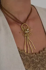 Collar con colgante dorado en forma de sol con perlas y cordón marrón.
